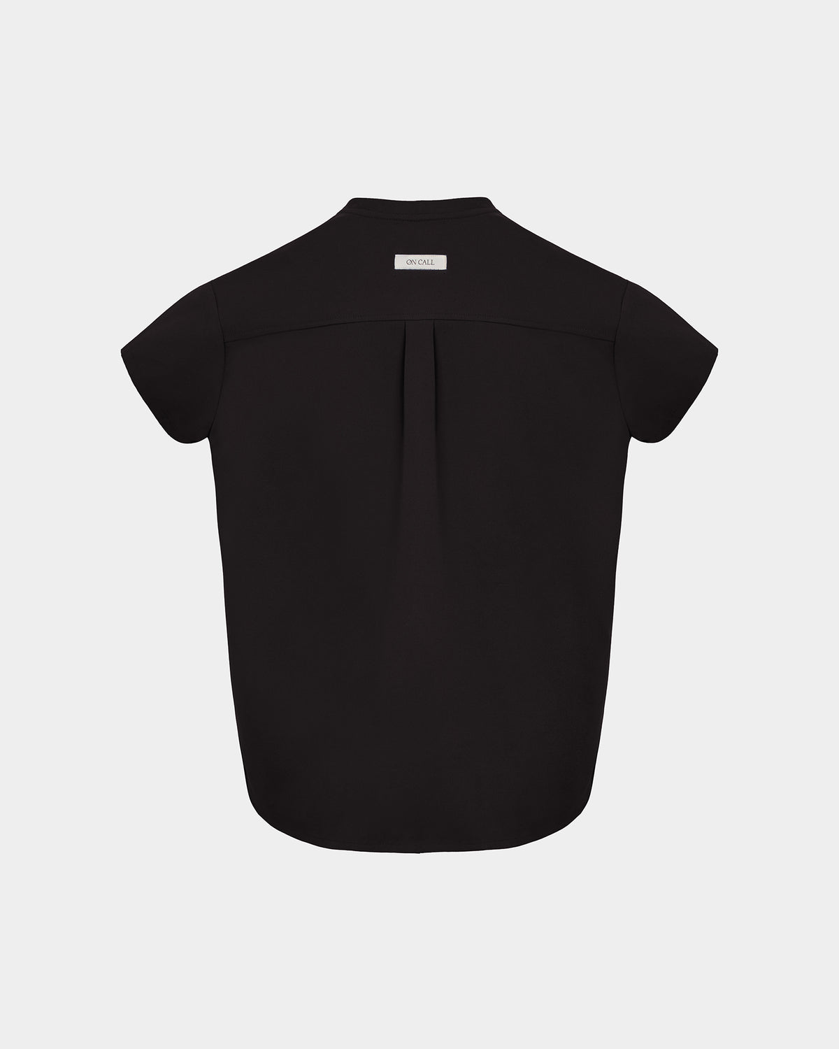 A black short-sleeve scrub shirt shown from the back, featuring a subtle center back pleat and a small white rectangular brand label at the collar, set against a light gray background.