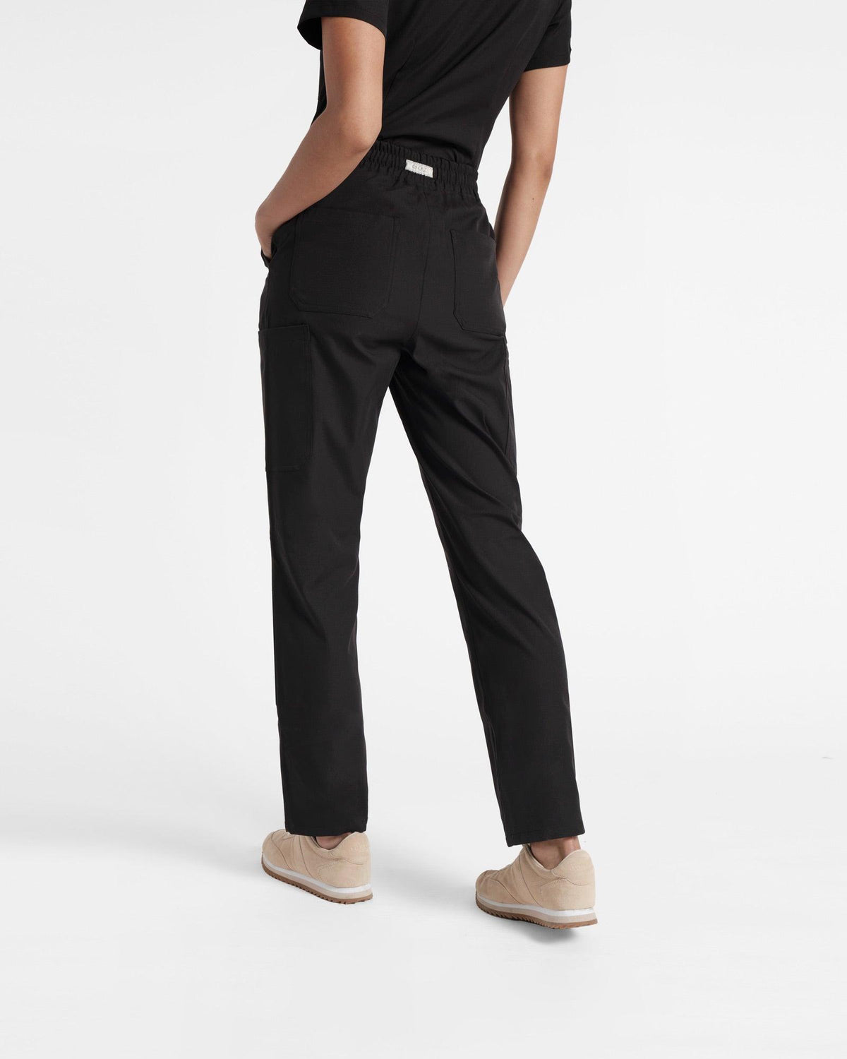 Back side view of women's black straight leg cargo scrub pants with two back pockets and branded fabric label at waistband.