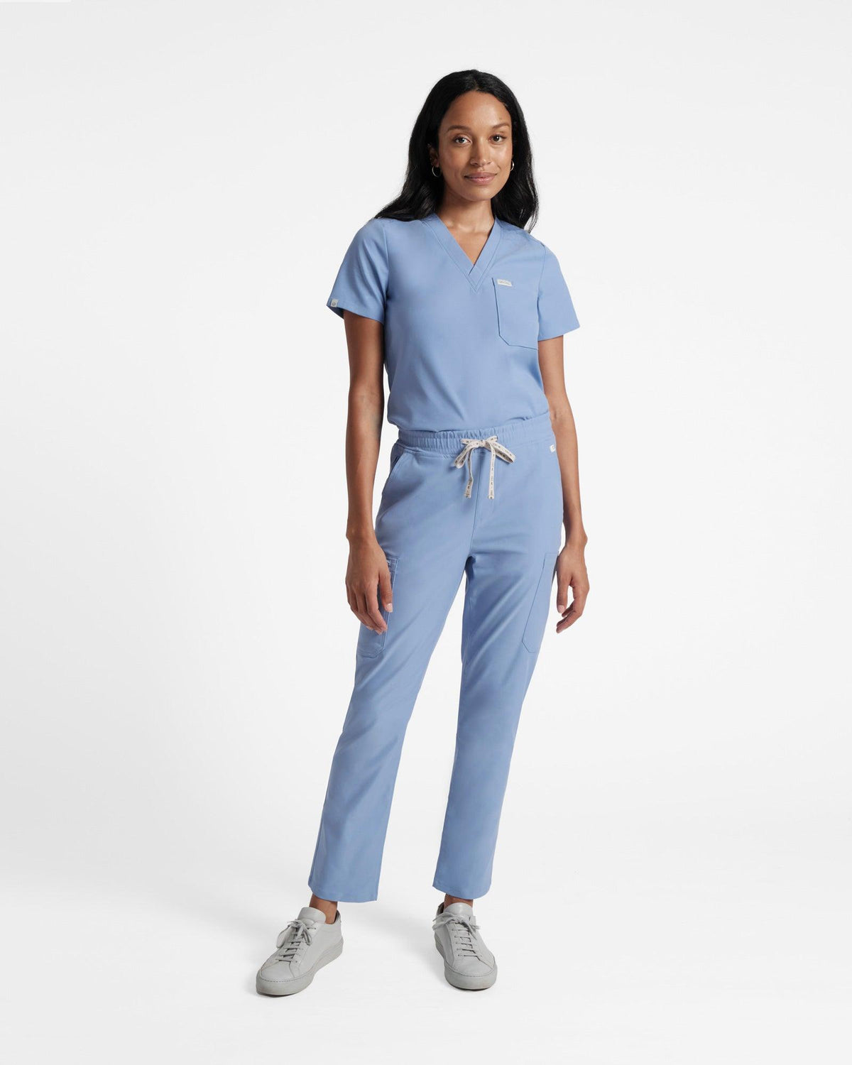 Woman wearing light blue cargo scrub pants with a matching v-neck scrub shirt tucked in.