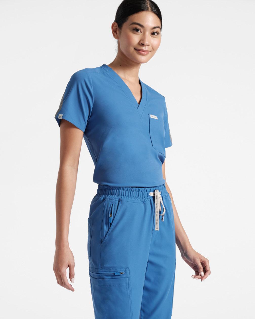 Angled view of woman in a bright blue scrub shirt tucked into matching cargo scrub pants.