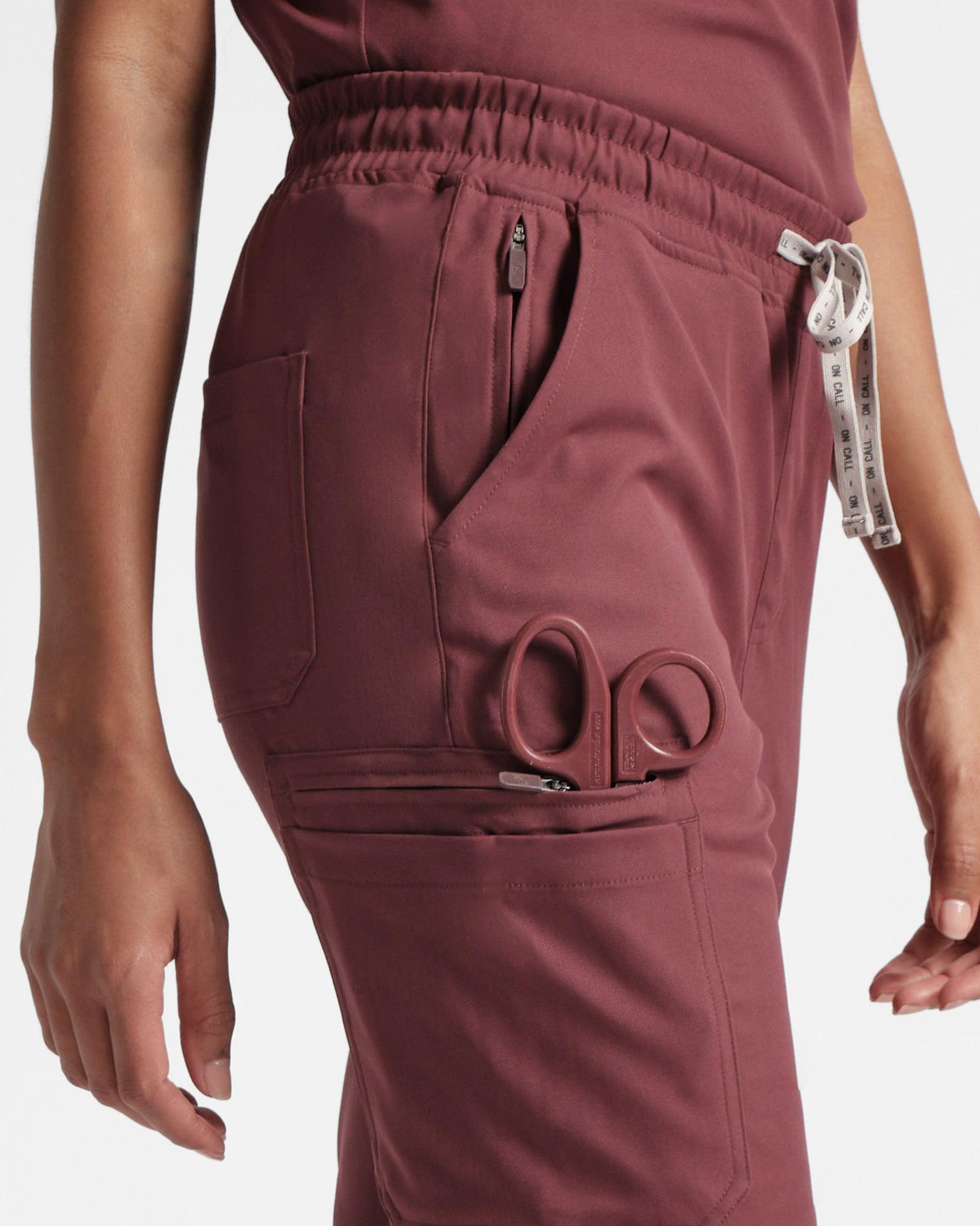 Detailed side view of woman's deep red cargo scrub pants, focused on side, waist, and back pockets.