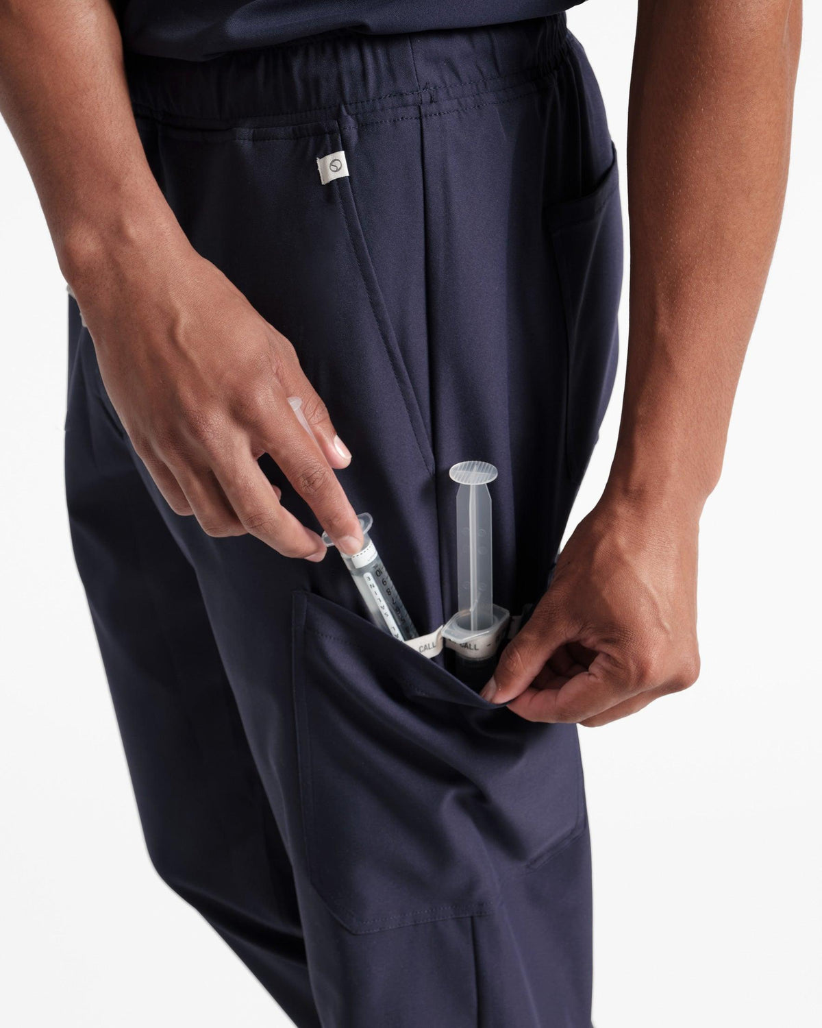 Detailed view of man reaching for syringes inside of his navy cargo scrub leg pocket.