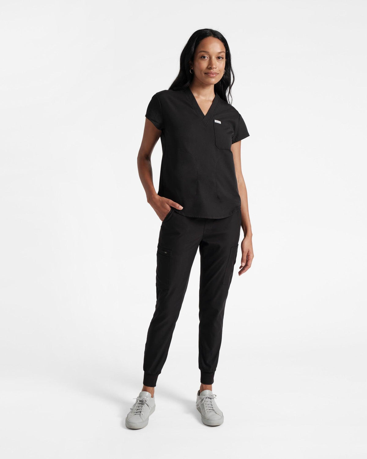 Full body view of woman in black v-neck scrub top with chest and side pockets and matching cargo jogger scrub pants.