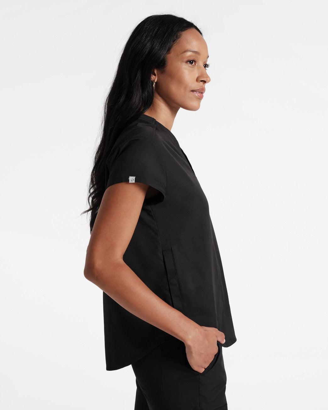 Side view of woman wearing black scrub top with branded On Call logo fabric label folded around sleeve hem.