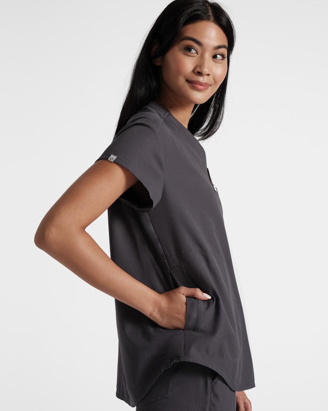Side view of woman wearing a dark grey scrub shirt with her hand in the shirt's side pocket.