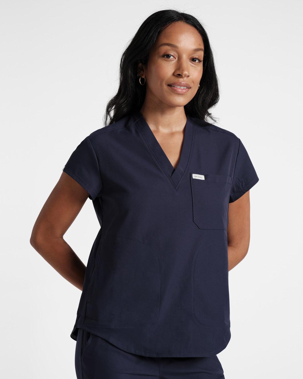 Woman in navy v-neck scrub top with hands folded behind her back.