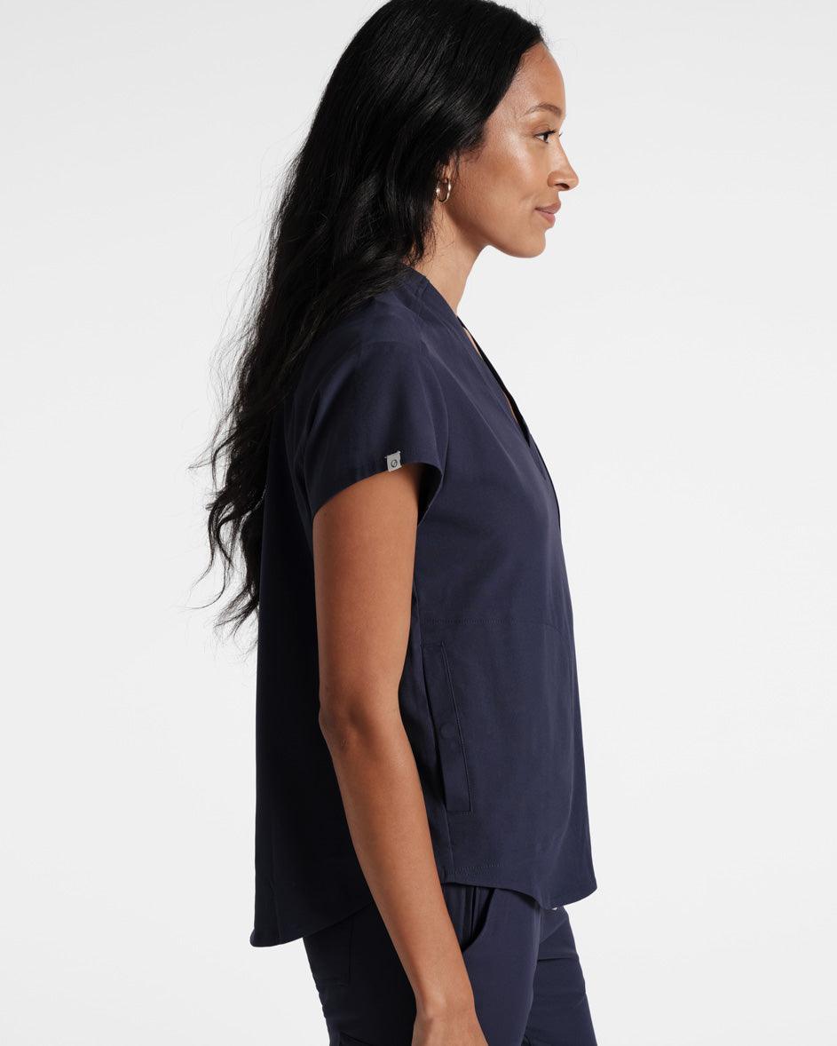 Side view of woman in navy scrubs with the shirt untucked over matching pants.