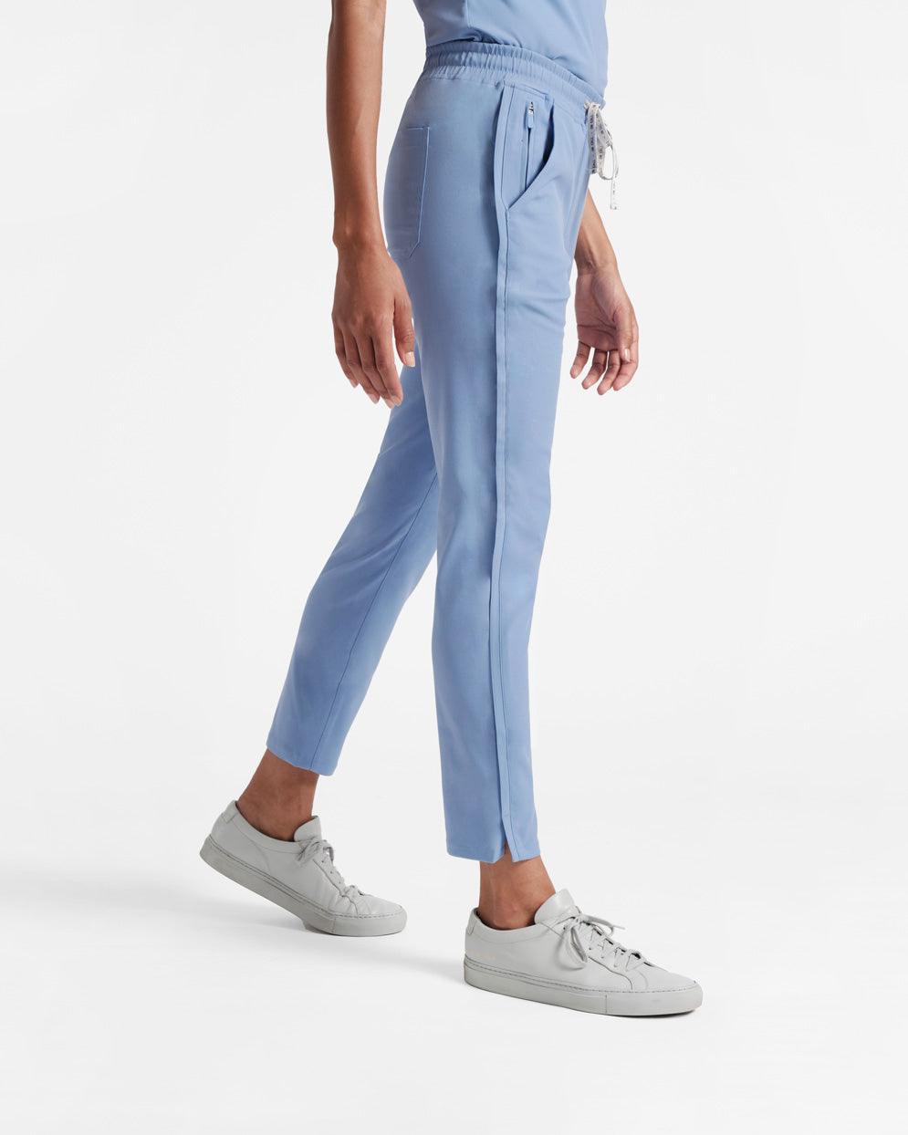 Side view of woman wearing light blue straight leg scrub pants with back, side, and hidden zipper pockets.