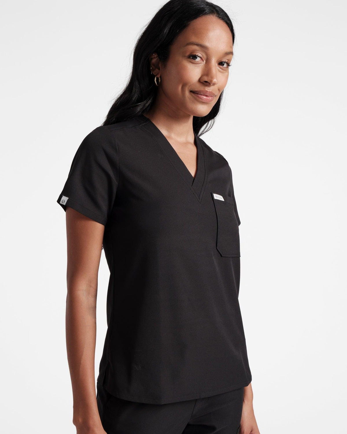 Angled front view of woman in black v-neck scrub top with chest pocket. Folded On Call logo fabric label on the sleeve hem.