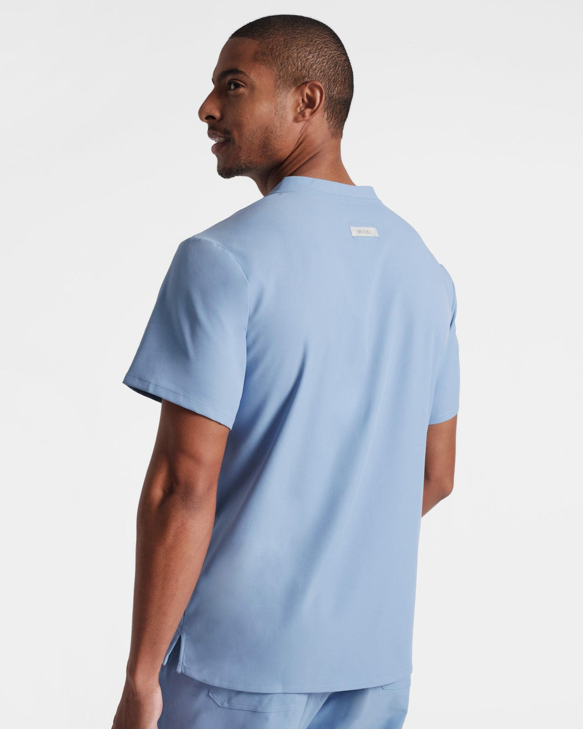 Angled back side view of man in light blue scrub shirt with an On Call fabric label sewn into the back.
