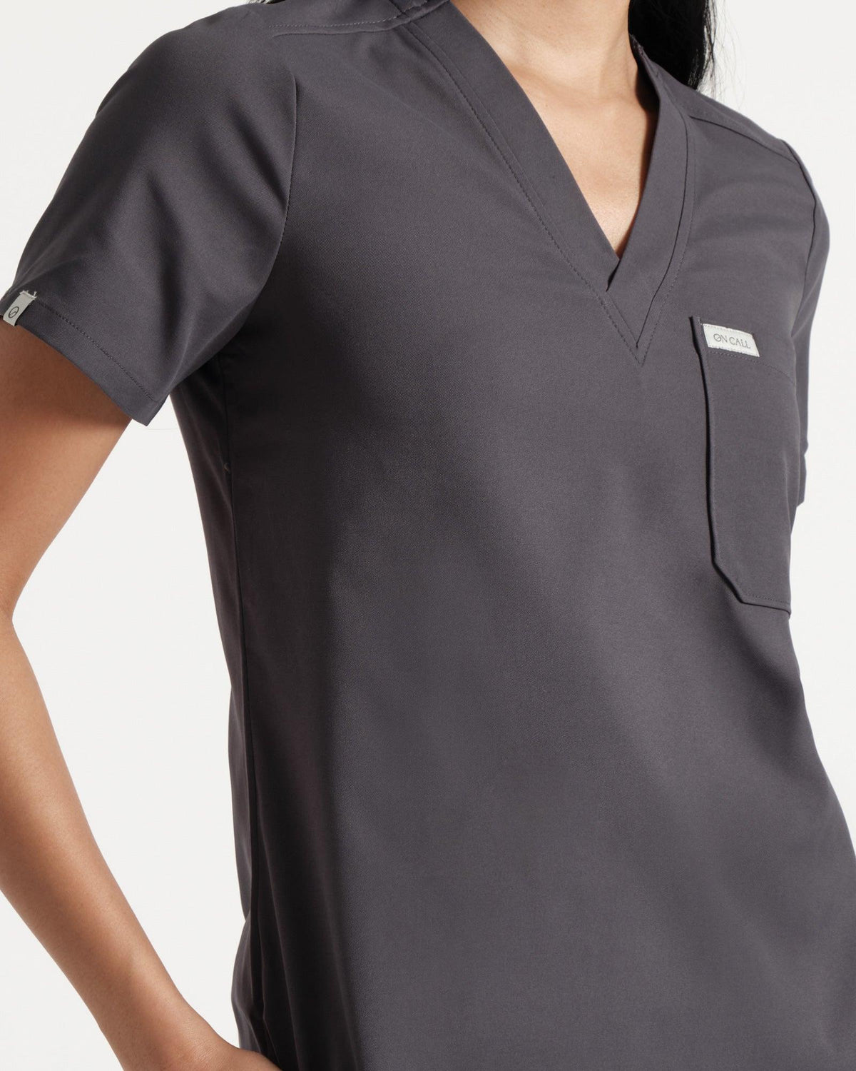 Angled front close up of woman's torso in a dark grey v-neck scrub shirt with a chest pocket.