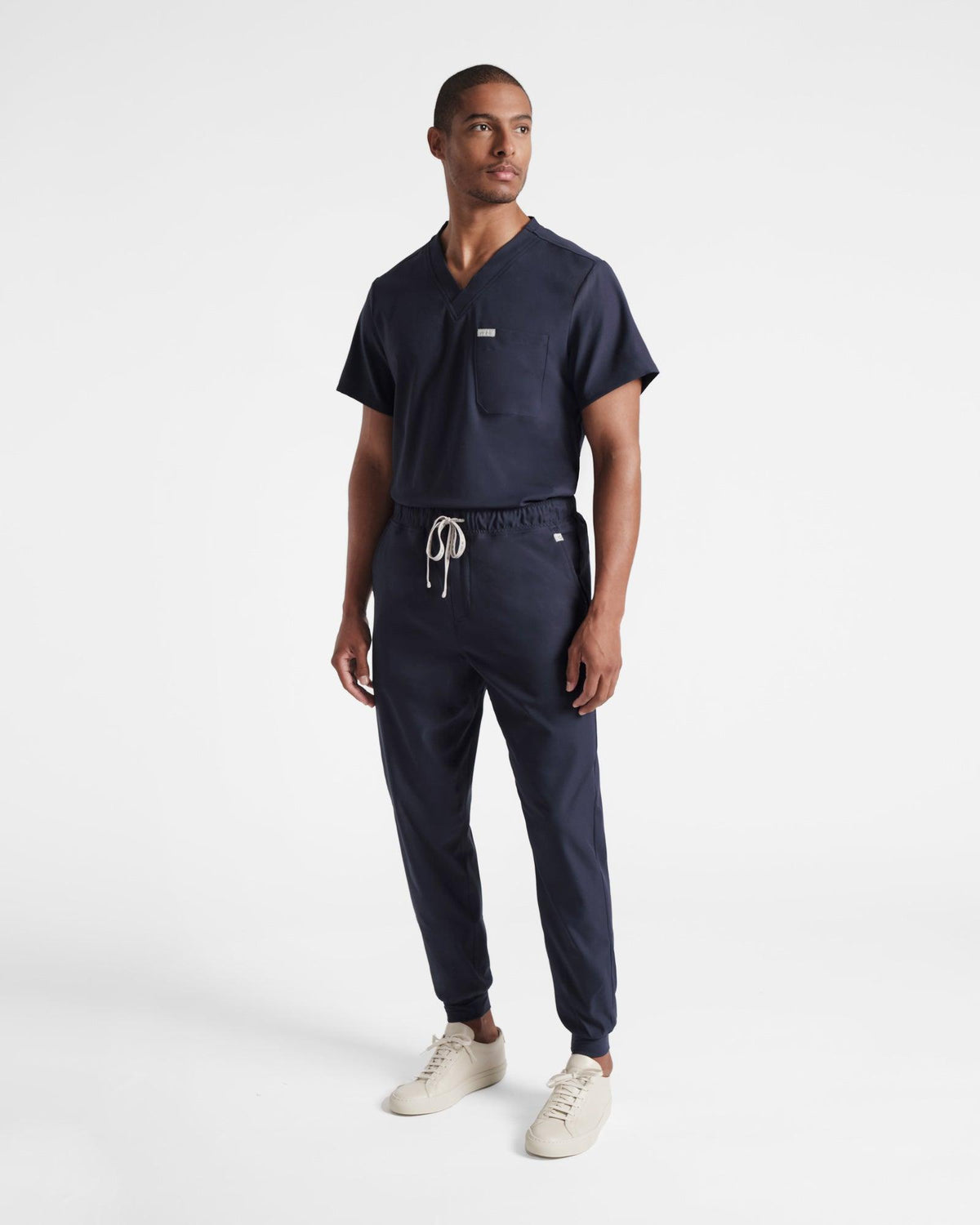 Man wearing a classic v-neck navy scrub shirt tucked into matching jogger scrub pants.
