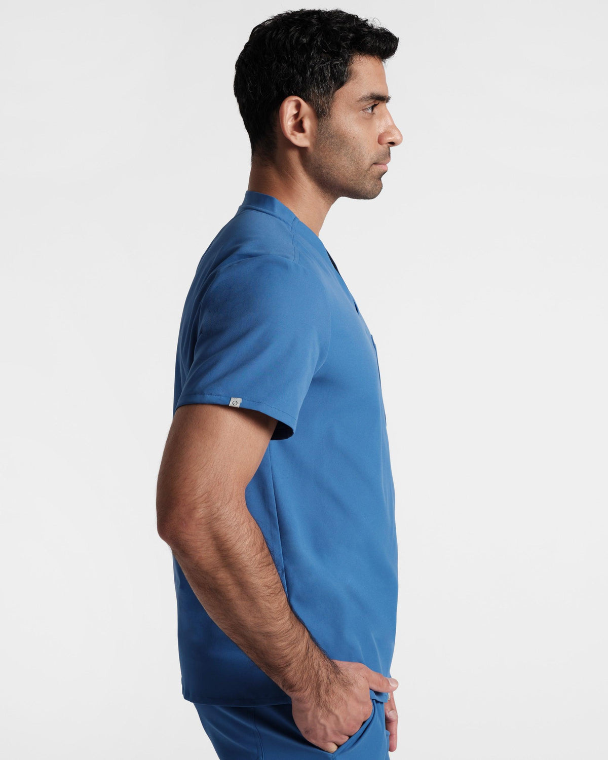 Side view of man wearing a bright blue scrub shirt with a small On Call emblem logo label wrapped around the sleeve hem.