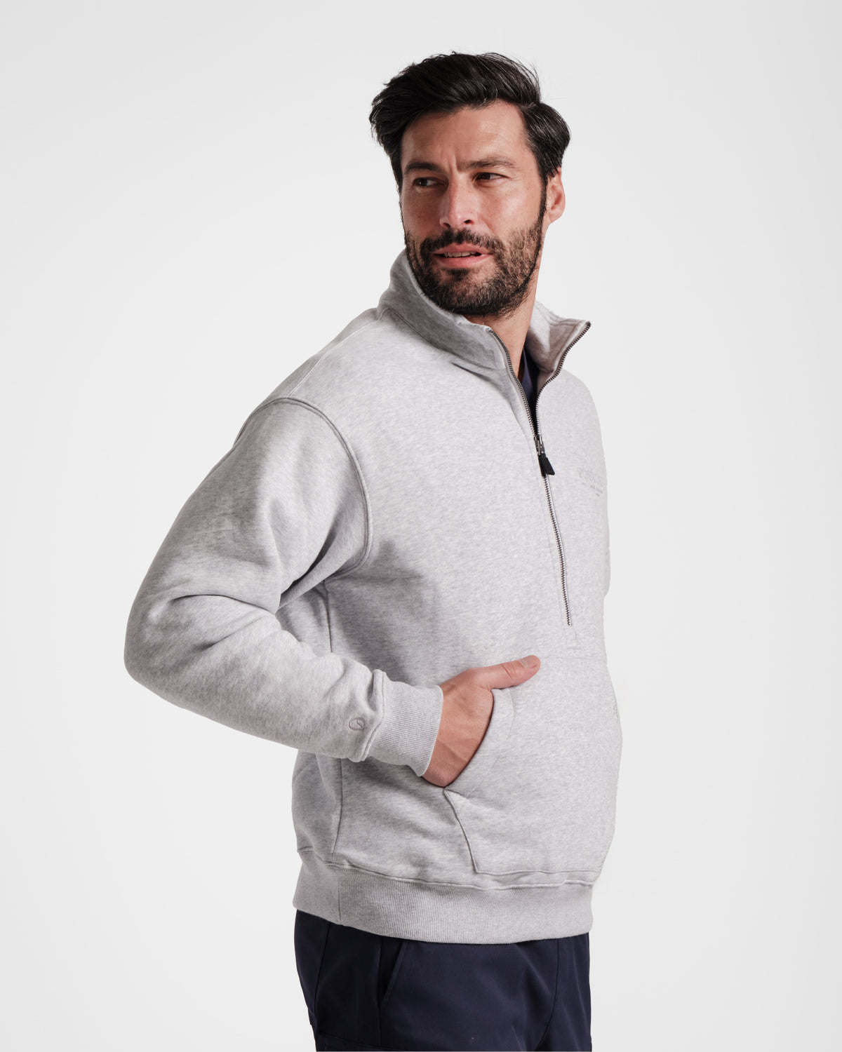 Angled view of man wearing heather grey half zip sweatshirt with his hand in the kangaroo pocket.