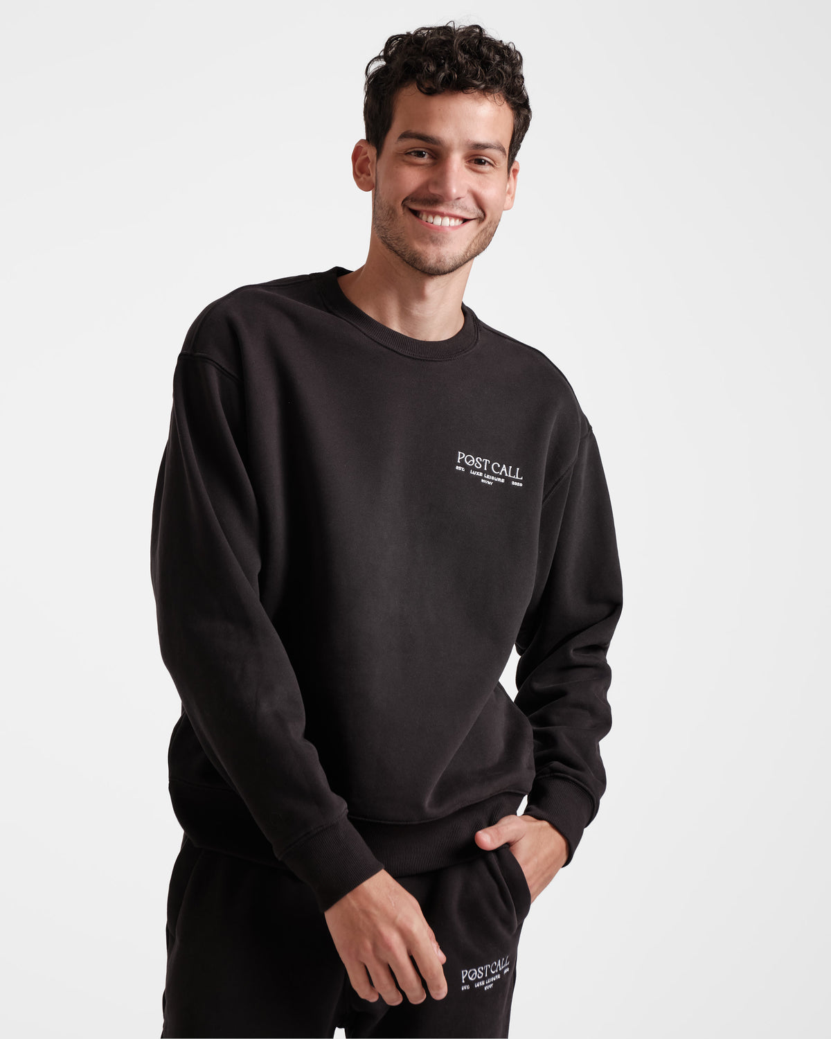 Man wearing black unisex crewneck sweatshirt with white embroidered Post Call logo on the left chest.