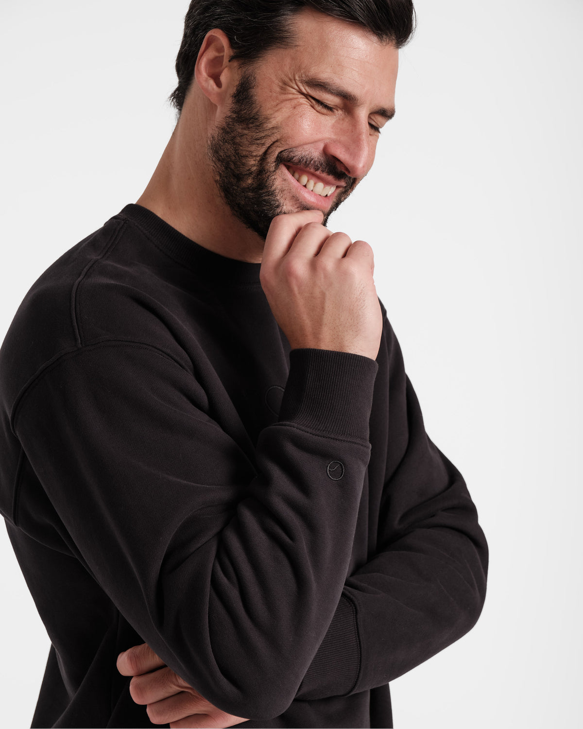 Man wearing unisex black crewneck sweatshirt with tonal Post Call emblem logo above wrist cuff.