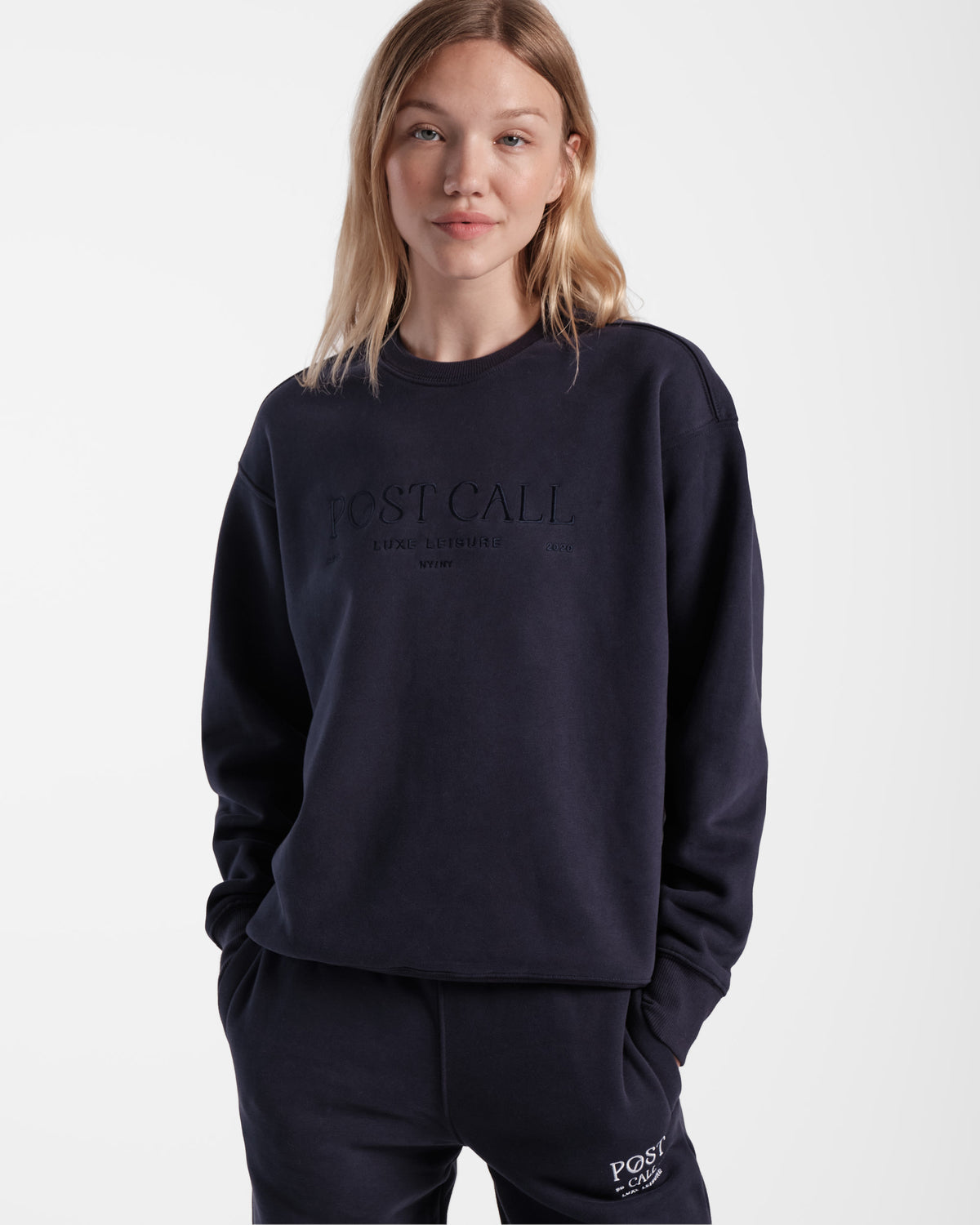 Woman wearing unisex navy crewneck sweatshirt with tonal Post Call logo embroidery across the chest.