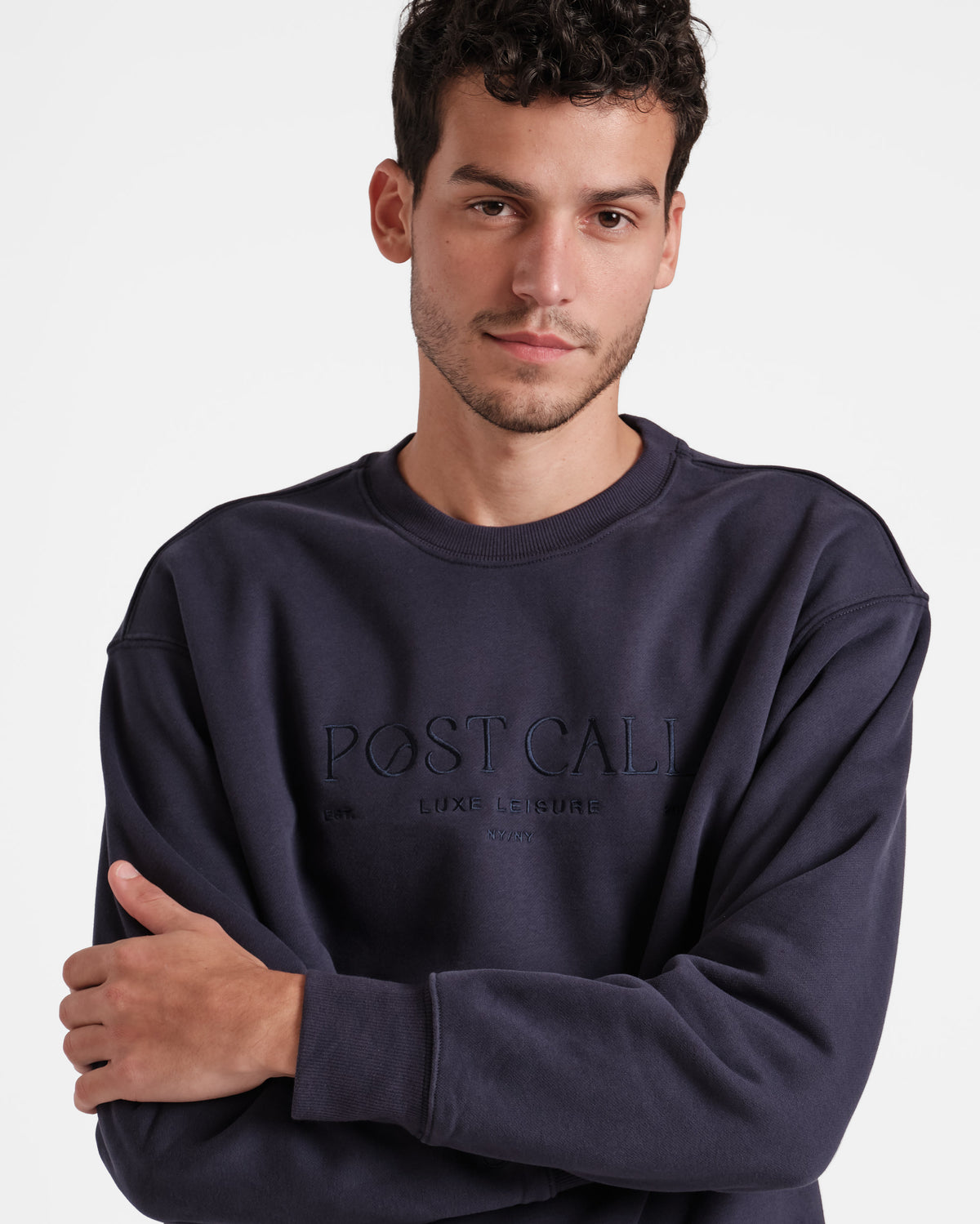 Man wearing unisex navy crewneck sweatshirt with tonal Post Call logo embroidery across the chest.
