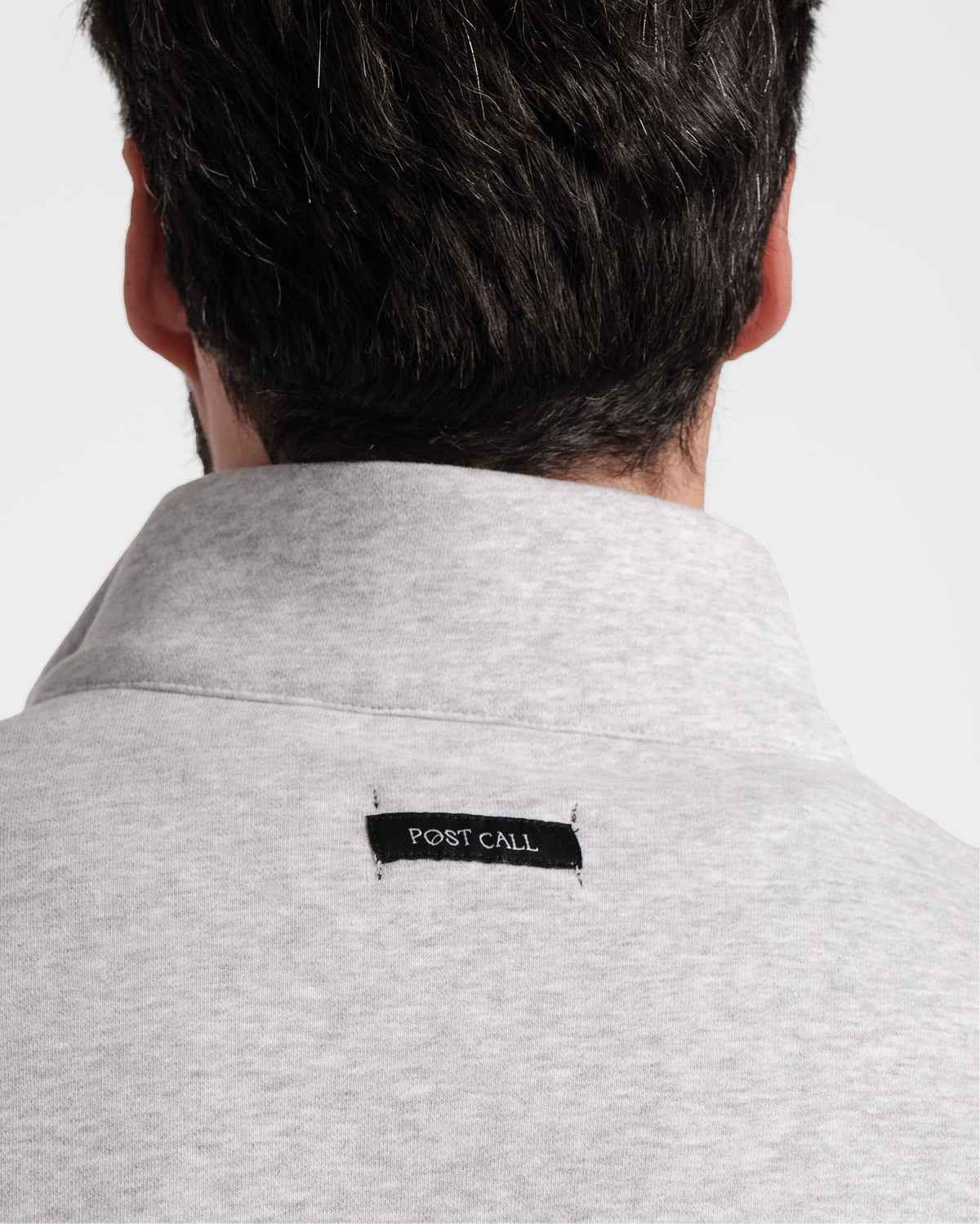 Close up view of Post Call fabric label sewn under the neck seam of a heather grey sweatshirt.