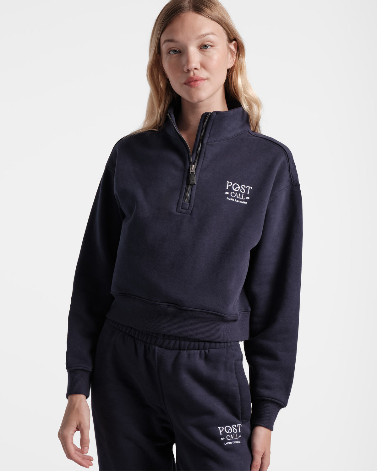 Woman wearing navy half zip sweatshirt with Post Call logo embroidered in white on the left chest.