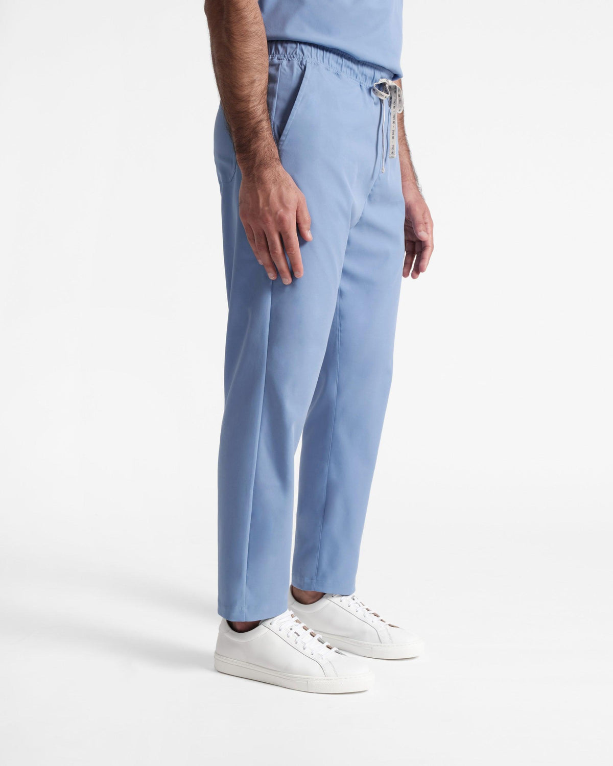 Side view of man in light blue straight leg scrubs with a branded drawstring at the waist.