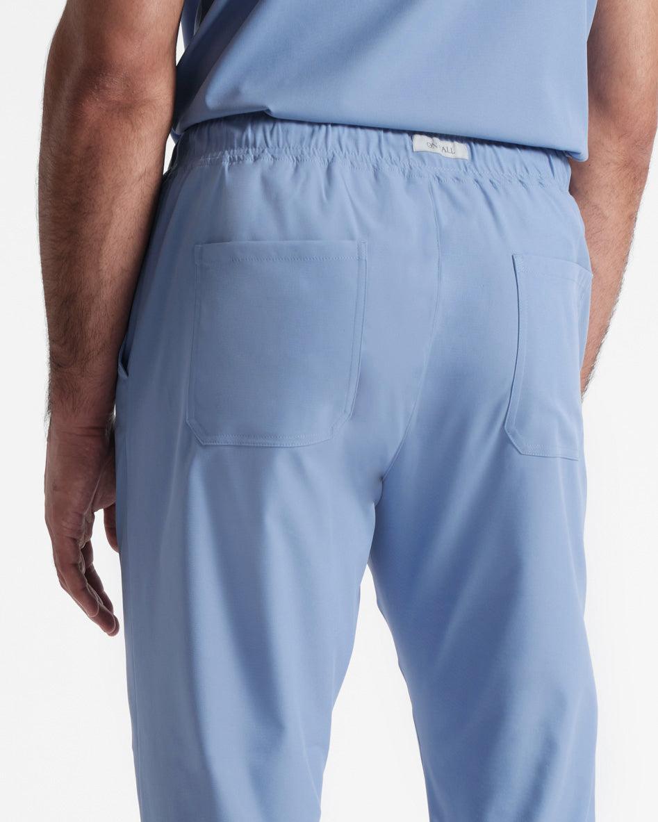 Close up back side view of man in light blue scrub pants with two back pockets and branded fabric label sewn into the elasticated waistband.
