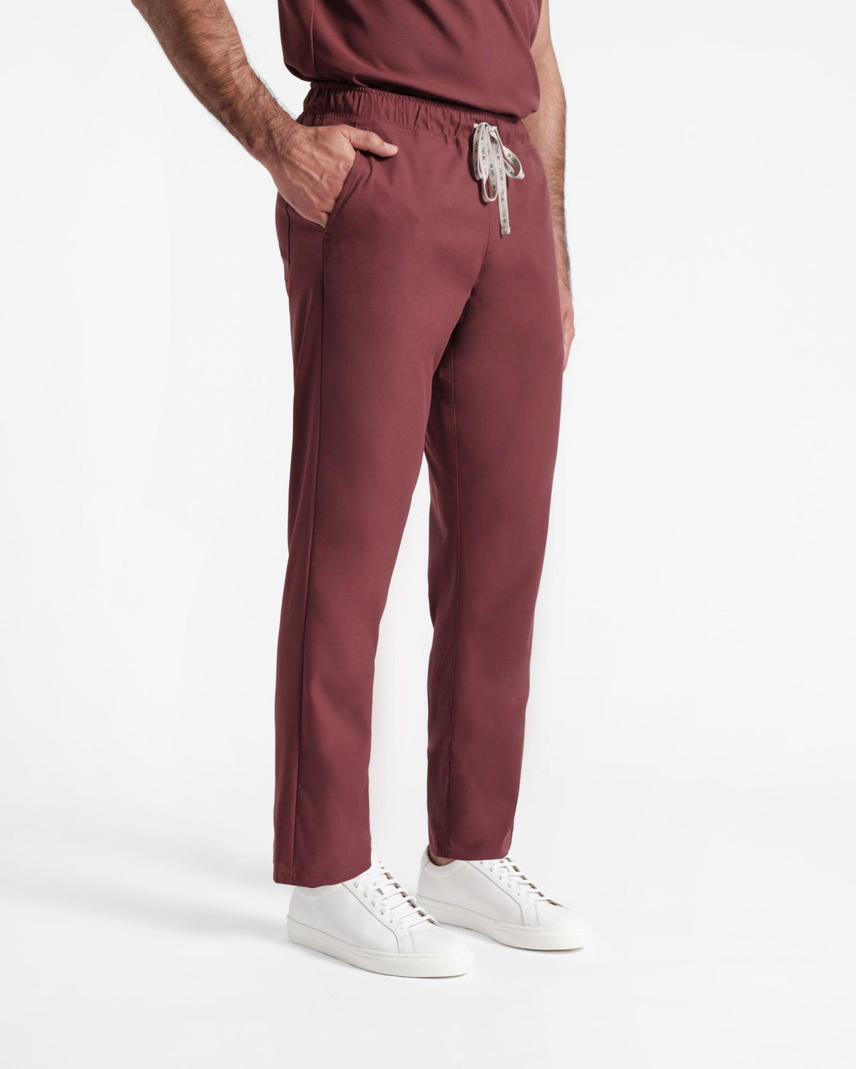 Angled side view of man in deep red straight leg scrub pants with a branded drawstring tie and hand in pocket.