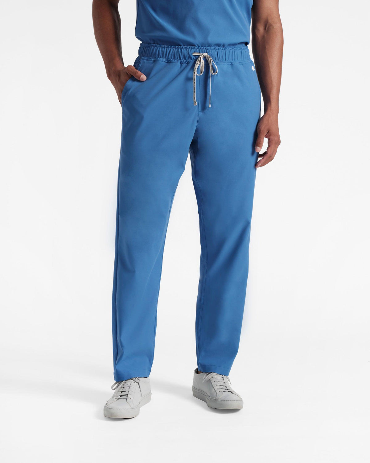 Man from the waist down in bright blue straight leg scrub pants with a branded drawstring.