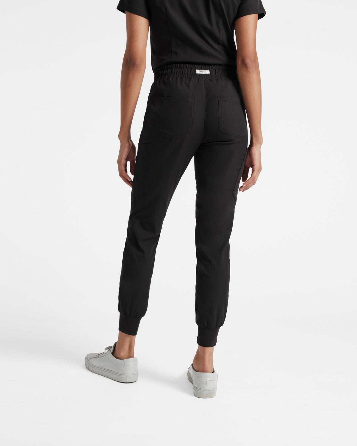 Back side view of black cargo jogger scrub pants with branded label at the waistband.
