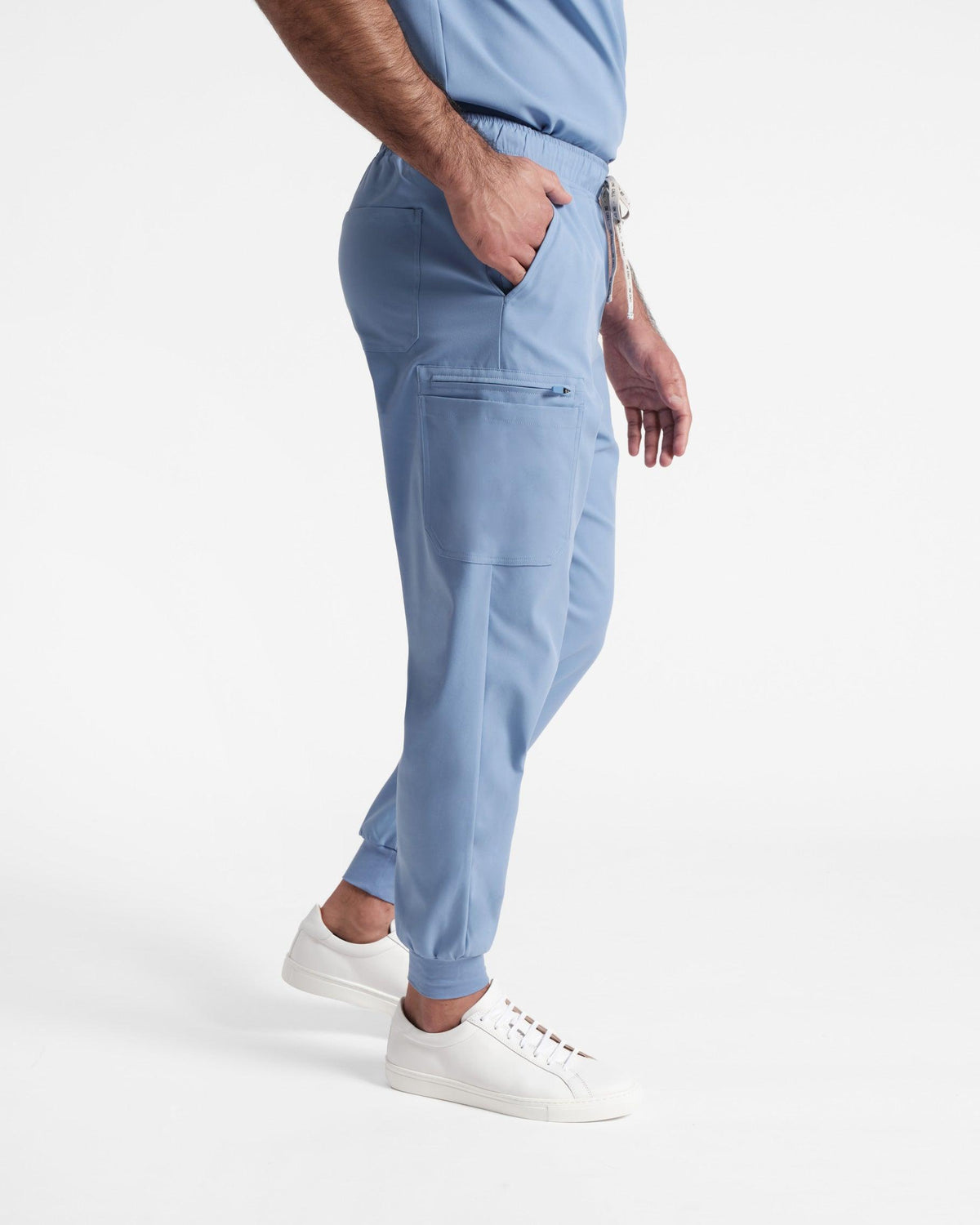 Side view of man in light blue jogger cargo scrubs with hand in waist pocket.