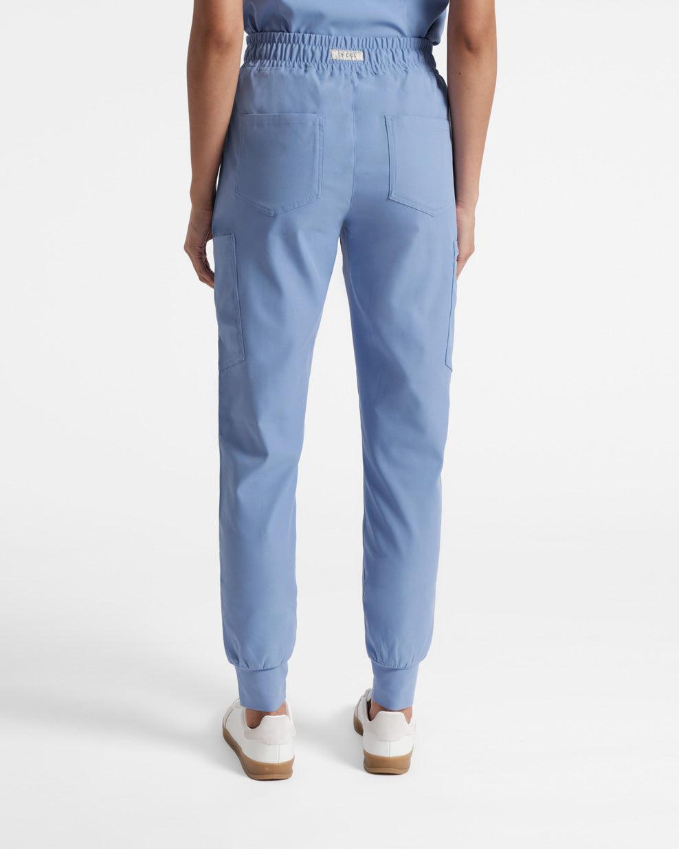 Back side view of woman wearing light blue cargo jogger scrub pants with two back pockets and On Call fabric logo label sewn into the outer waistband.