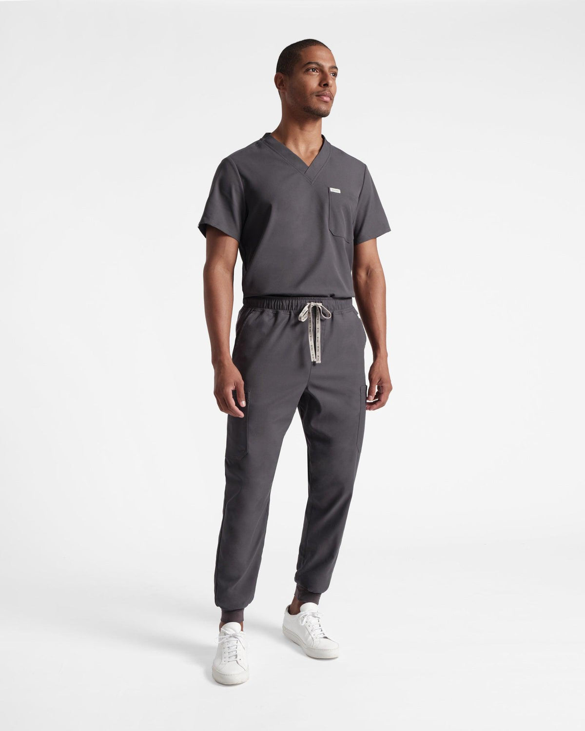 A man in dark grey cargo jogger scrub pants and a matching v-neck scrub shirt tucked in.