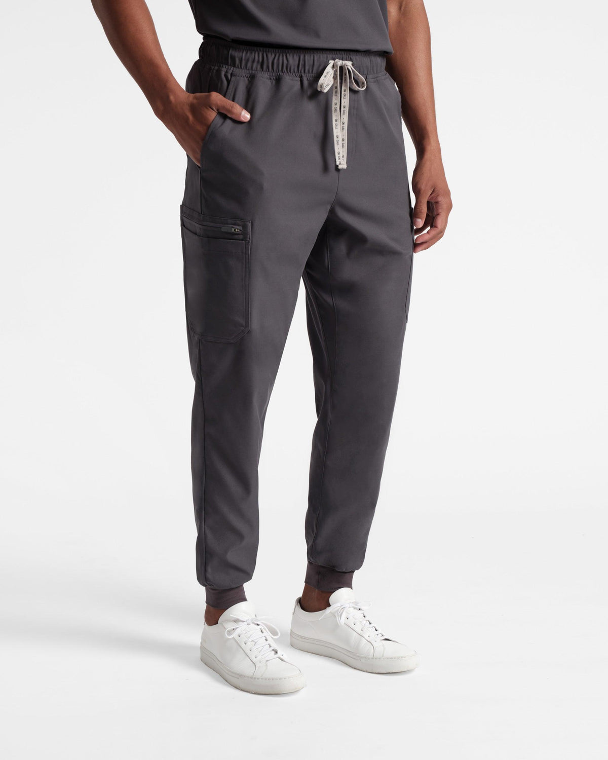 A man wearing dark grey jogger scrub pants with multiple pockets and ankle cuffs.