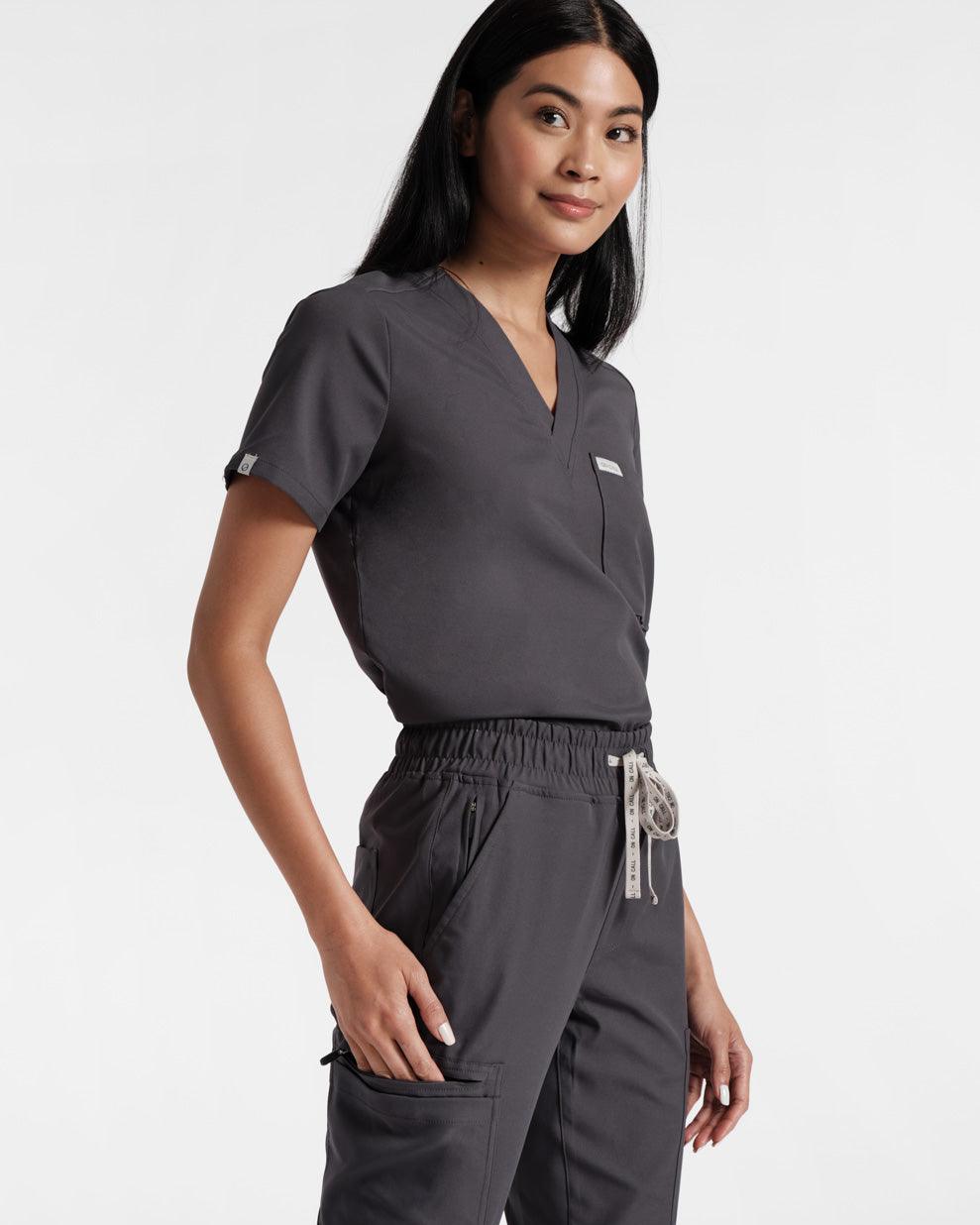 Angled side view of woman in dark grey cargo scrub pants with a matching v-neck top tucked in.