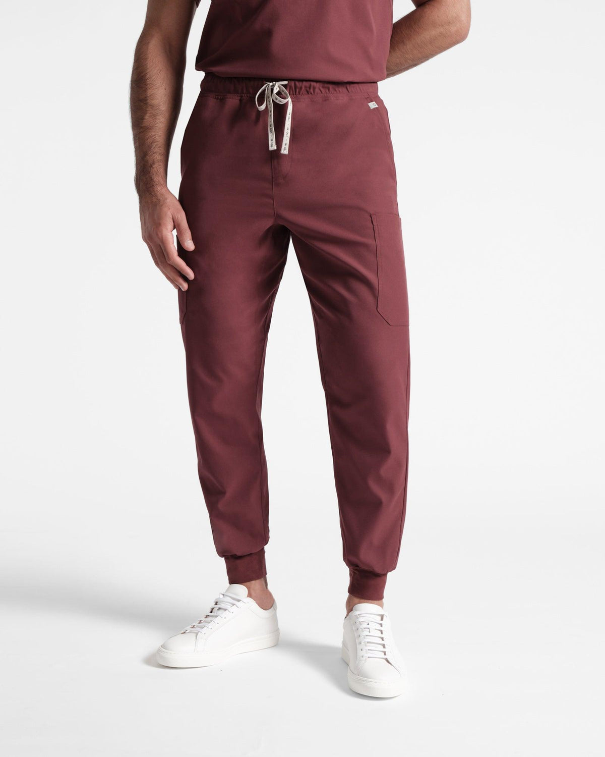 Man in deep red cargo jogger scrub pants with soft ribbed ankle cuffs, one hand resting at his side, and the other behind his back.