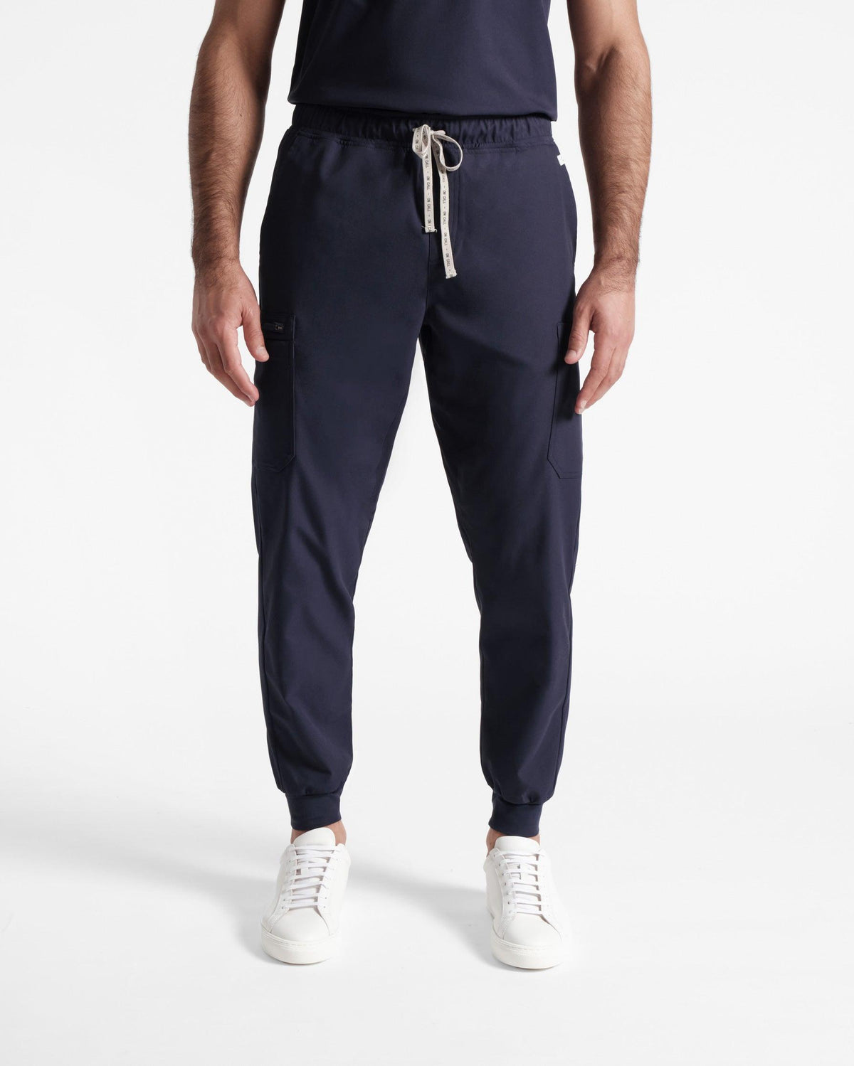 A man standing, wearing navy jogger cargo scrub pants with soft ribbed ankle cuffs.