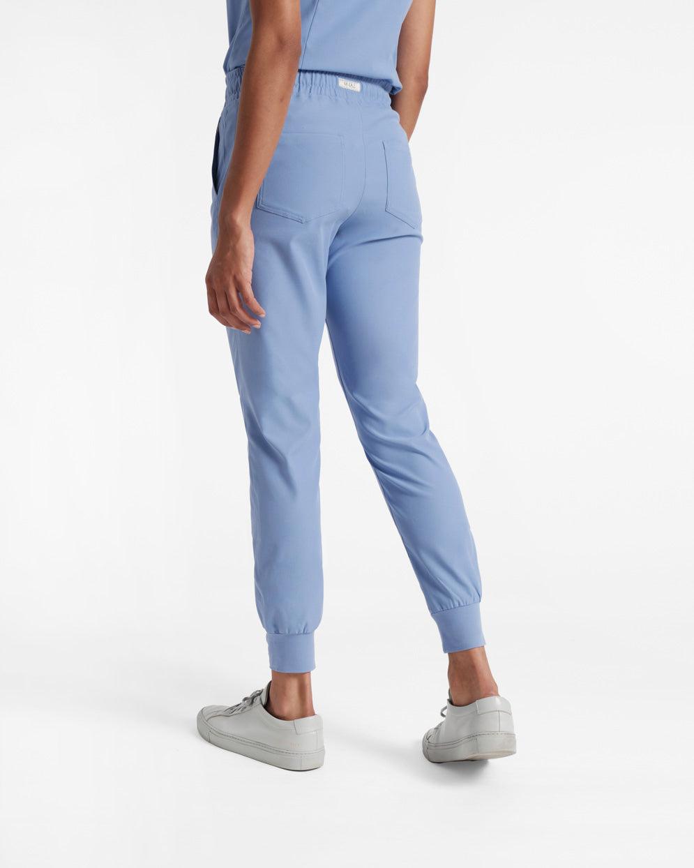 Angled back view of a woman in light blue jogger scrub pants with soft ribbed ankle cuffs.