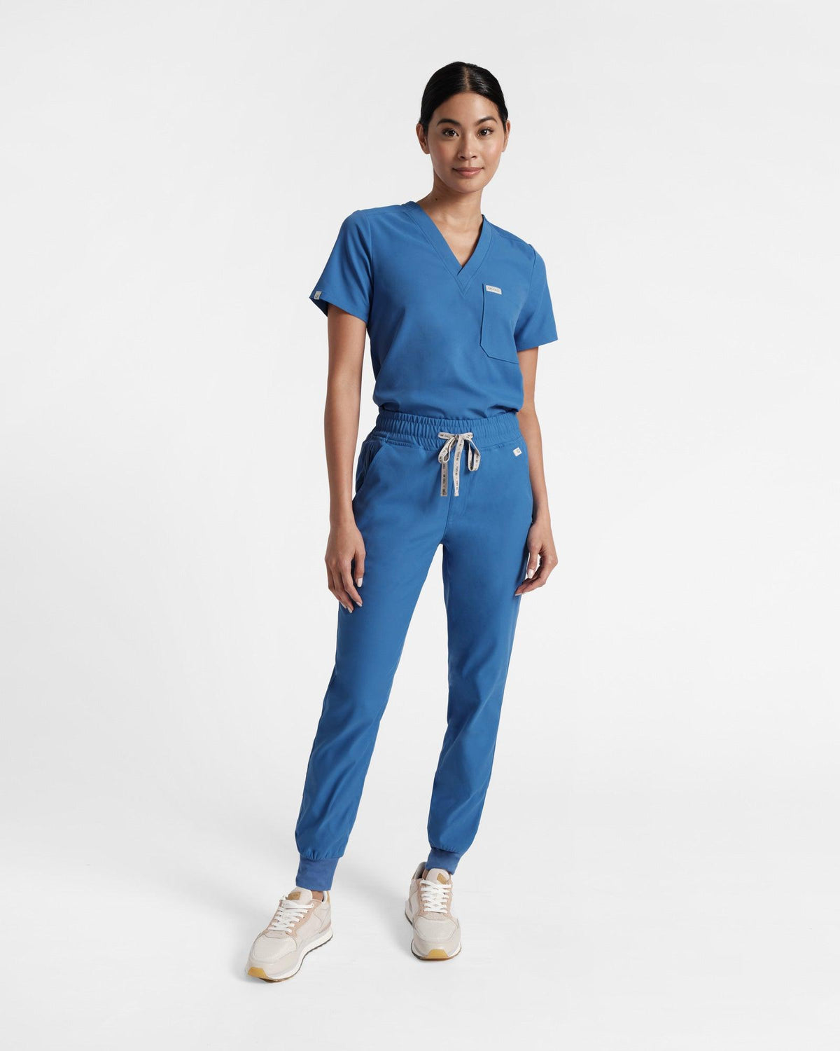 Woman in bright blue jogger scrub pants and a matching v-neck top tucked in.