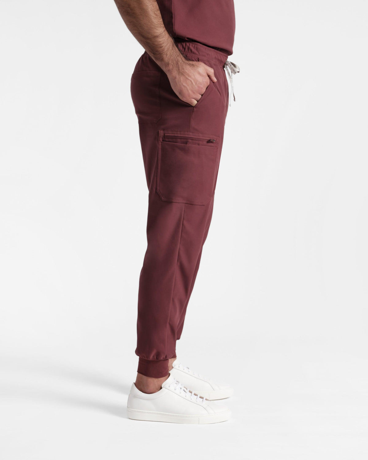 Side view of man in deep red cargo jogger scrub pants with his hand in the waist pocket.