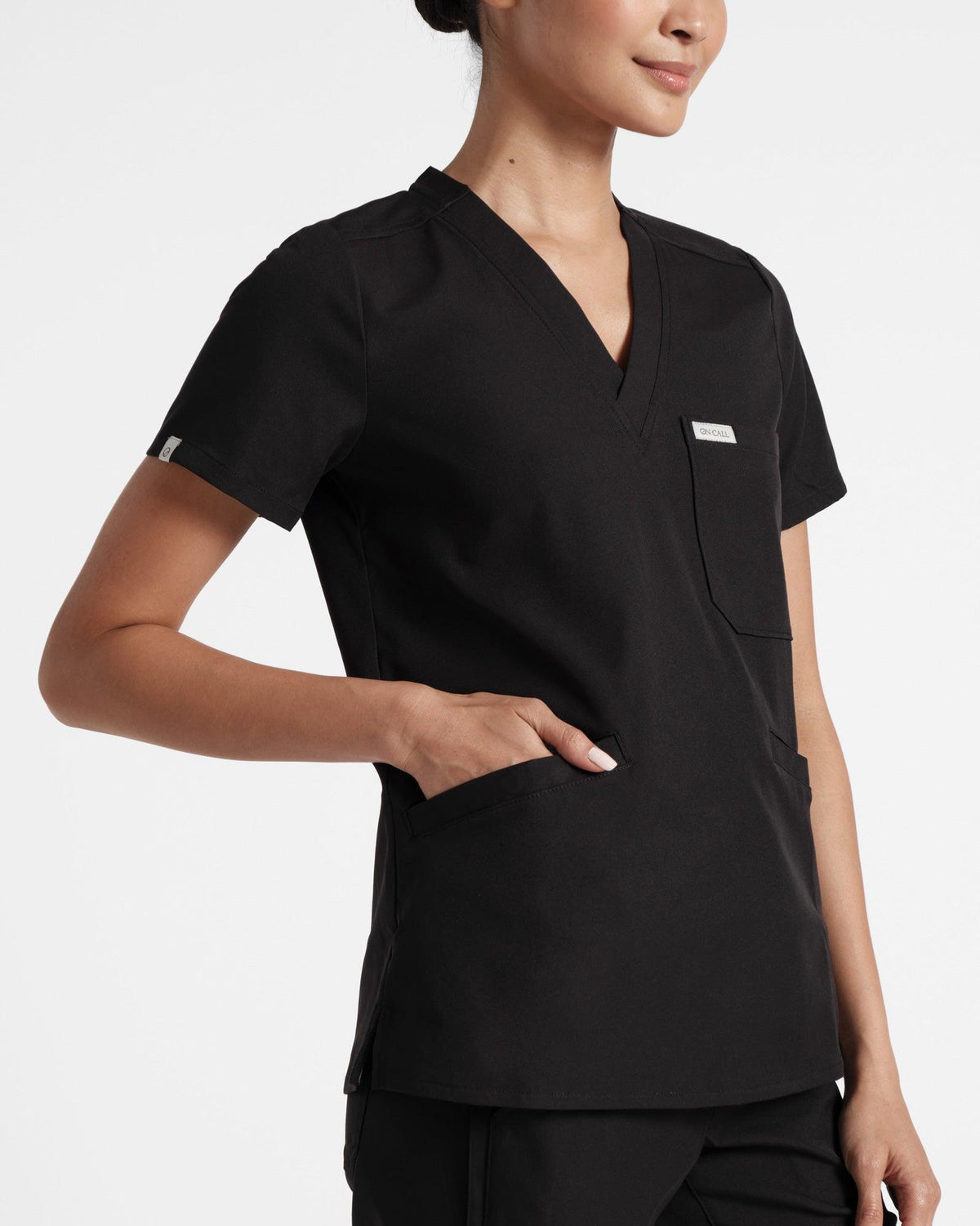Angled view of a three pocket black scrub top.