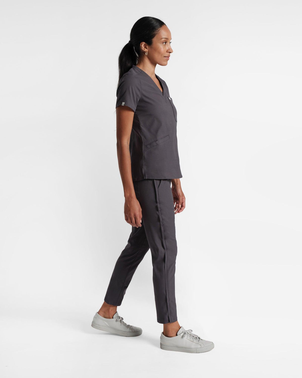 Side view of woman in a dark grey scrub shirt with a v-neck and matching straight leg pants with a small ankle slit.