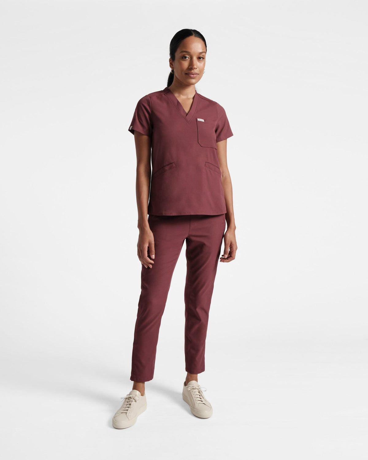 Woman in a deep red matching scrub set with a v-neck shirt and straight leg pants.