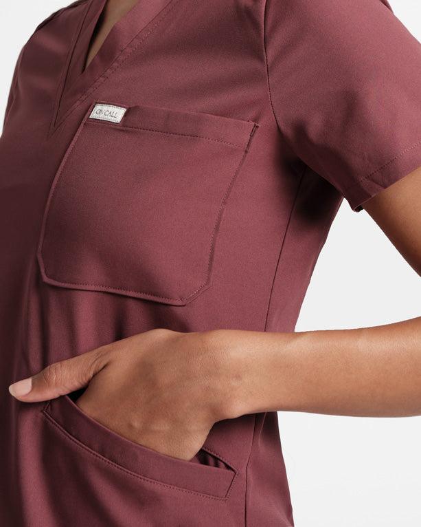 Close up view of woman wearing a deep red scrub shirt with chest pocket and hand in one of the front pockets.