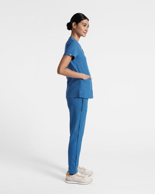 Side view of woman in bright blue scrubs with her hand in the front shirt pocket.
