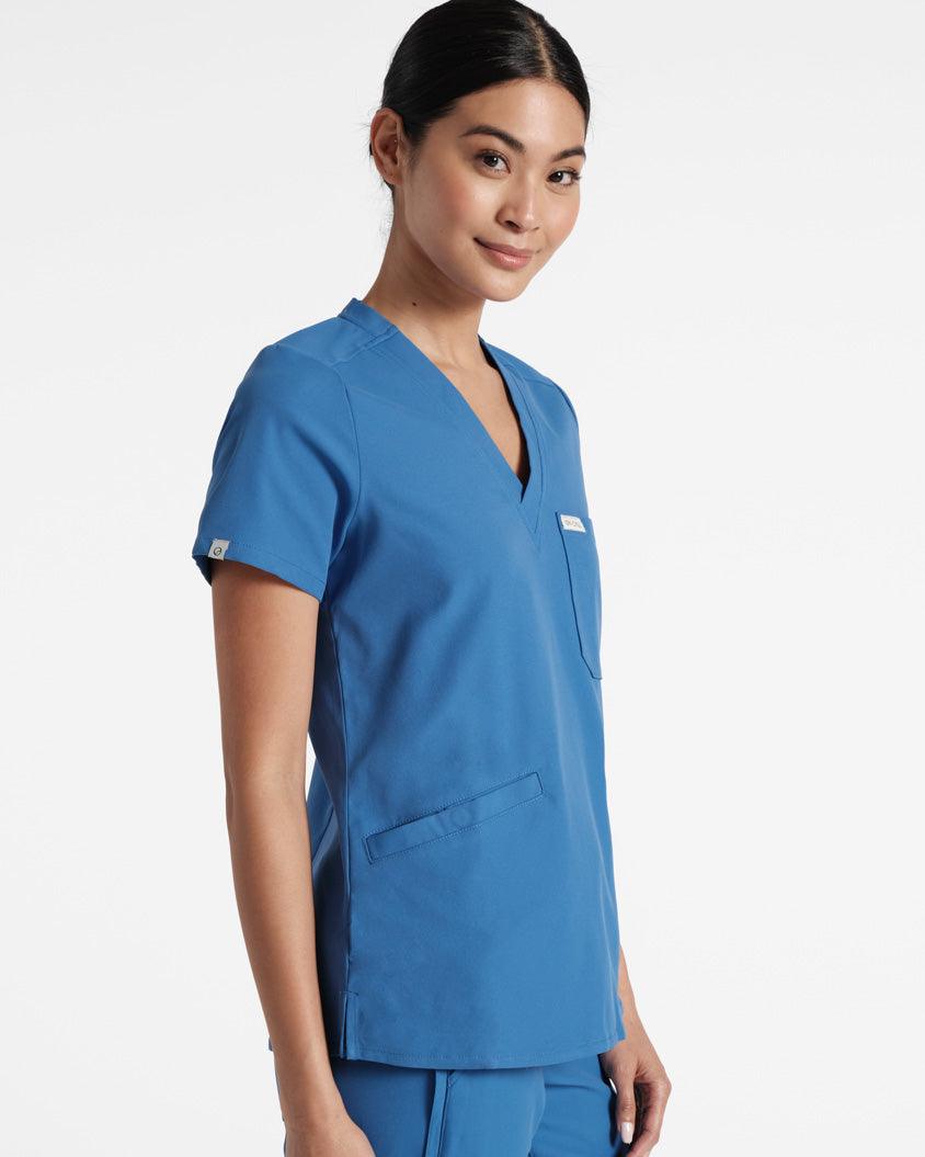Angled front view from the upper thighs up of a woman in bright blue scrubs with front pockets.