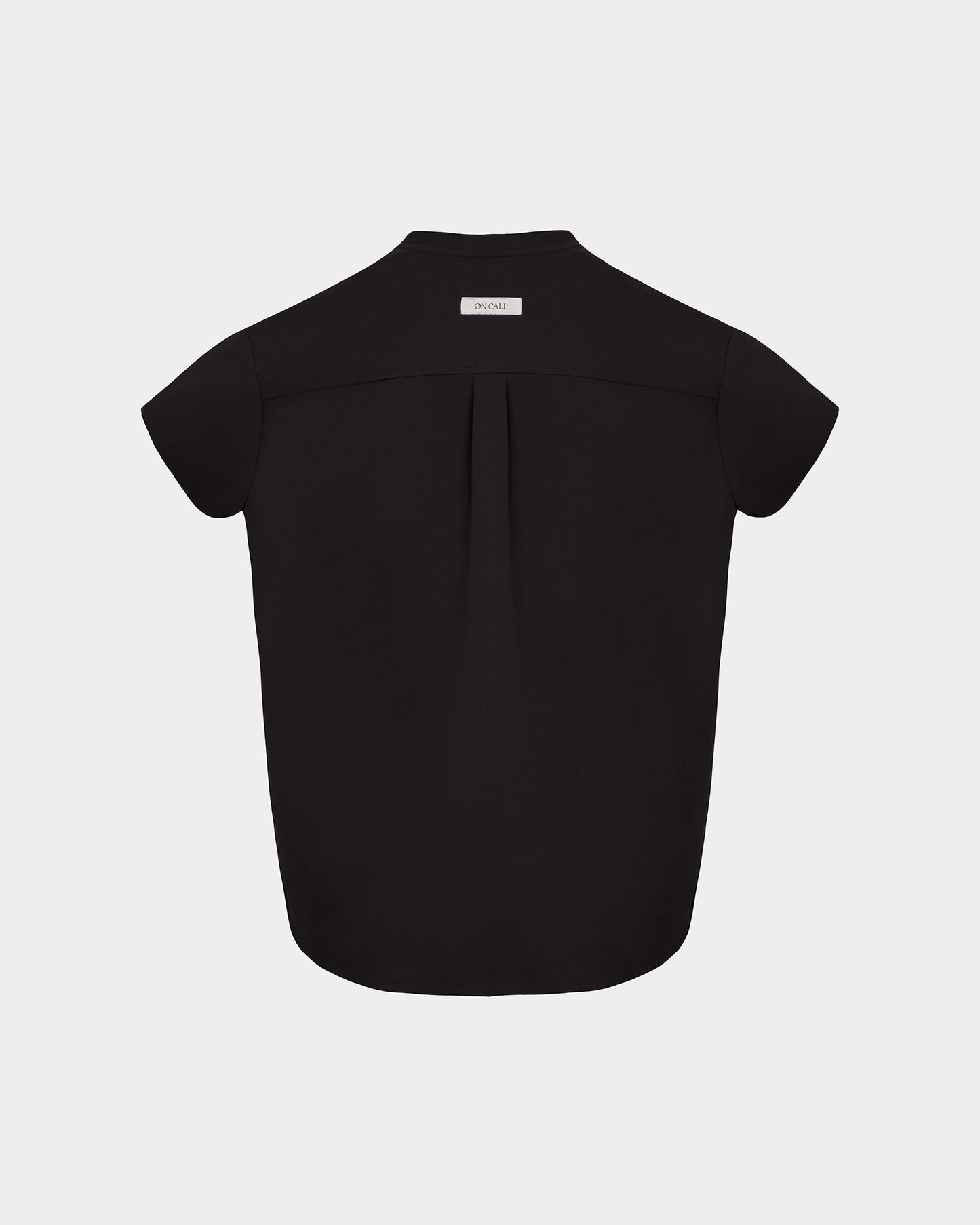 A black short-sleeve scrub shirt shown from the back, featuring a subtle center back pleat and a small white rectangular brand label at the collar, set against a light gray background.