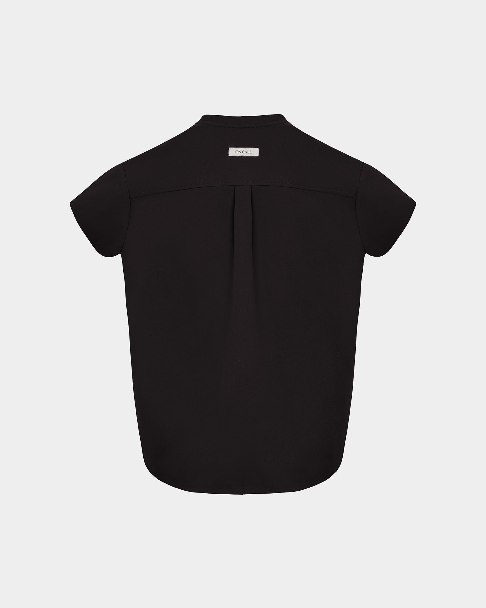 A black short-sleeve scrub shirt shown from the back, featuring a subtle center back pleat and a small white rectangular brand label at the collar, set against a light gray background.