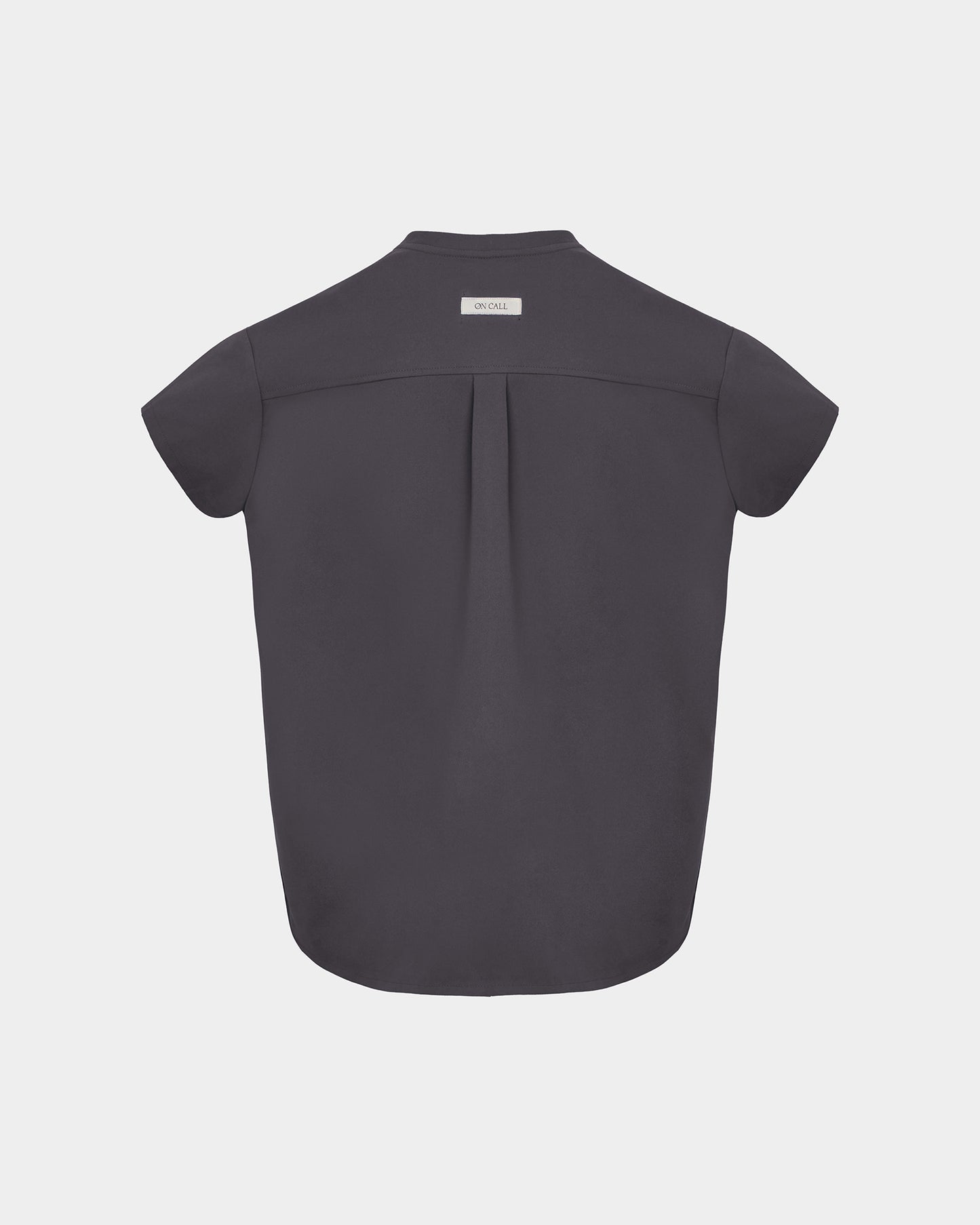 A dark grey short-sleeve scrub shirt shown from the back, featuring a subtle center back pleat and a small white brand label at the collar, set against a light gray background.