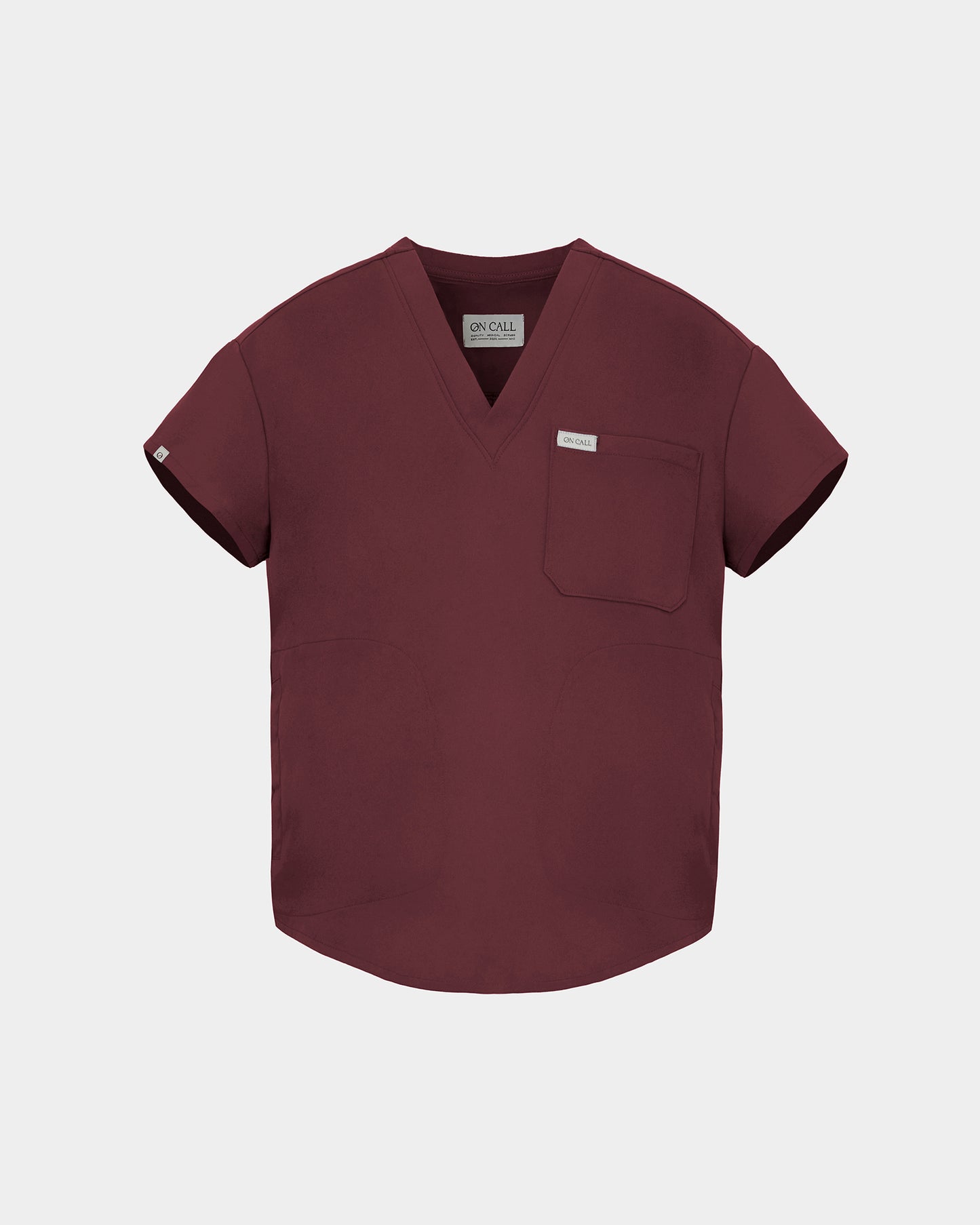 A short-sleeve V-neck scrub top in a deep heme red color, featuring a chest pocket with a small white label, displayed on a light gray background.