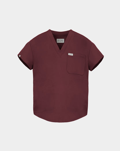 A short-sleeve V-neck scrub top in a deep heme red color, featuring a chest pocket with a small white label, displayed on a light gray background.